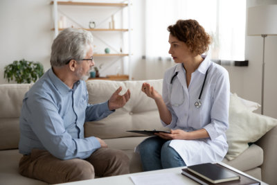 Young woman doctor sit on couch with senior old lady patient